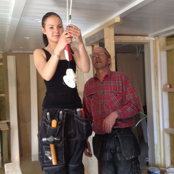 To ansatte som monterer taklamper med verktøybelte på i et hus sim er i prosessen med å pusses opp